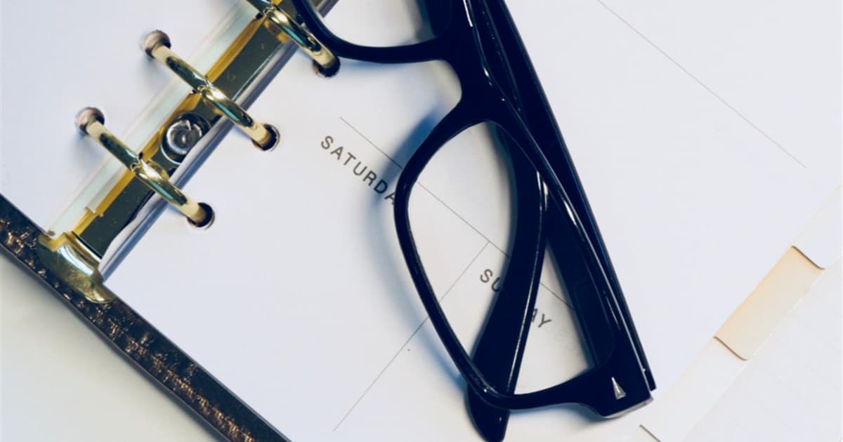 Weekly paper planner lying open with black reading glasses resting on the page