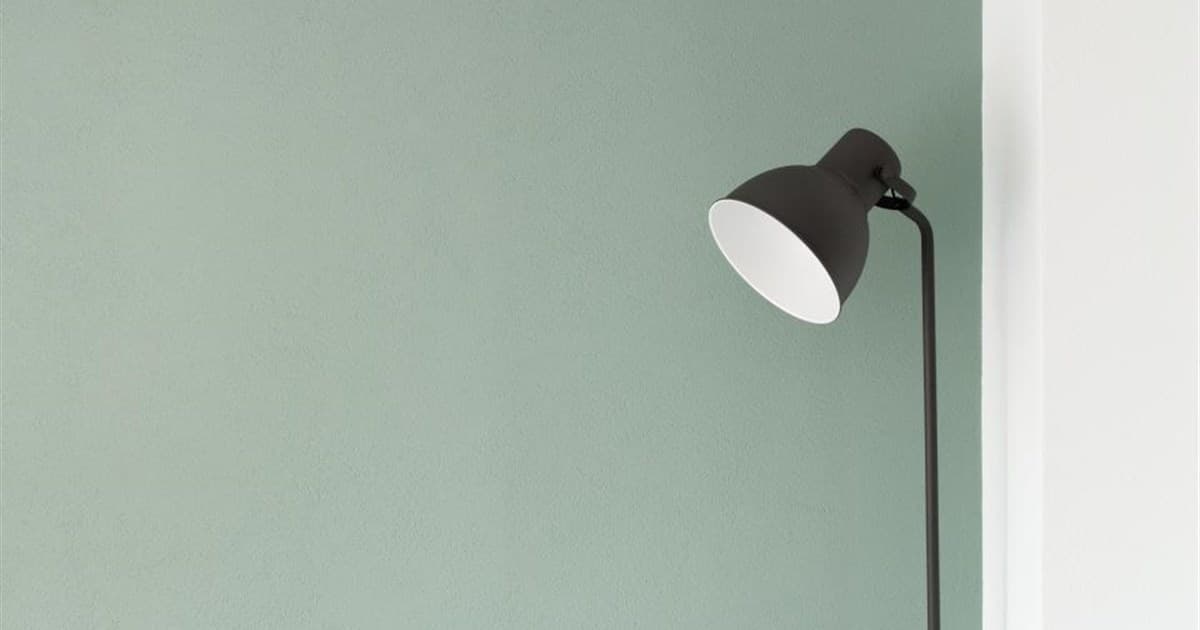Black floor lamp angled against a sage green wall beside a white doorway