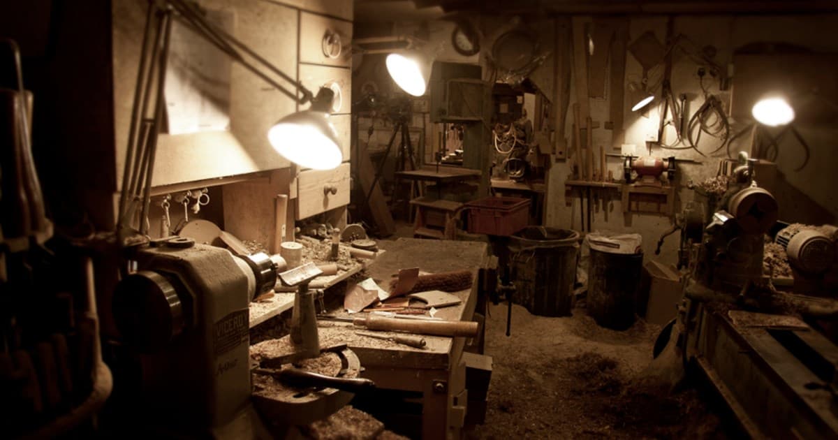 Dimly lit woodworking workshop with lathes, workbenches and hand tools on the walls