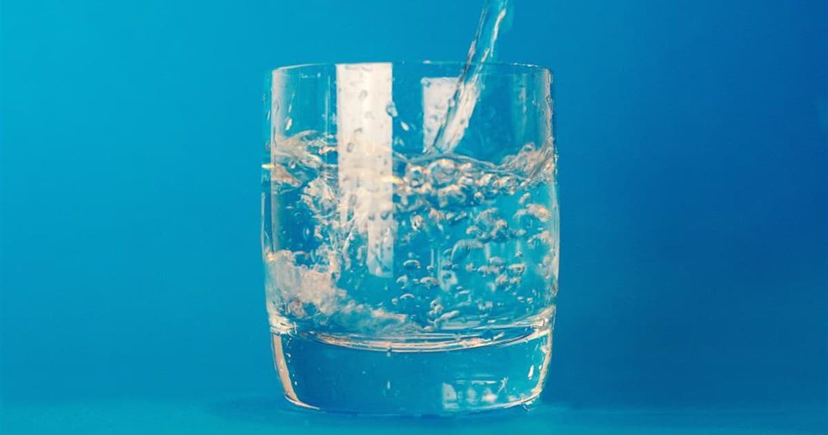 Water being poured into a clear tumbler against a deep blue background