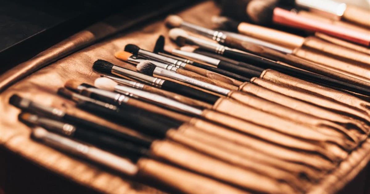 Row of makeup brushes lined up in an open tan leather brush roll