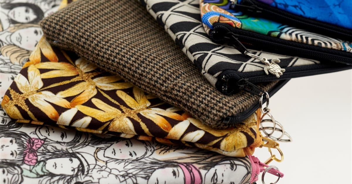 Stack of patterned fabric zip pouches with metal zip pulls and charms